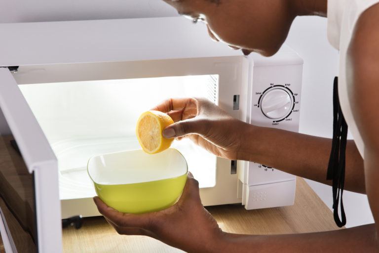 A woman placing a water with fresh lemon squeezed into it into the microwave.