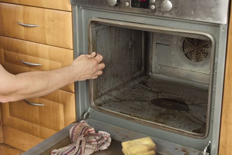 A person cleaning a very dirty oven.