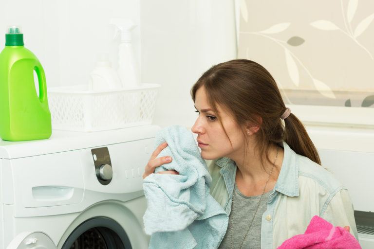 A woman tentatively sniffing laundry pulled from a washing machine.