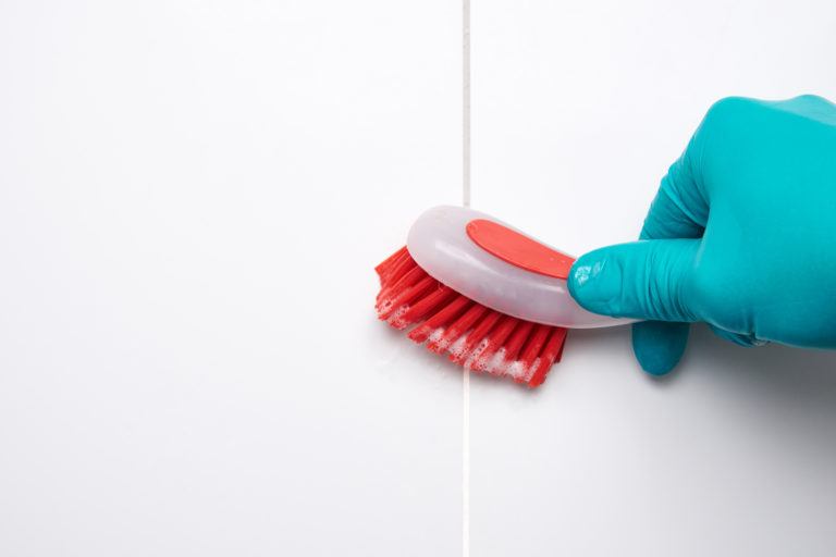 A gloved hand scrubbing bathroom tile.