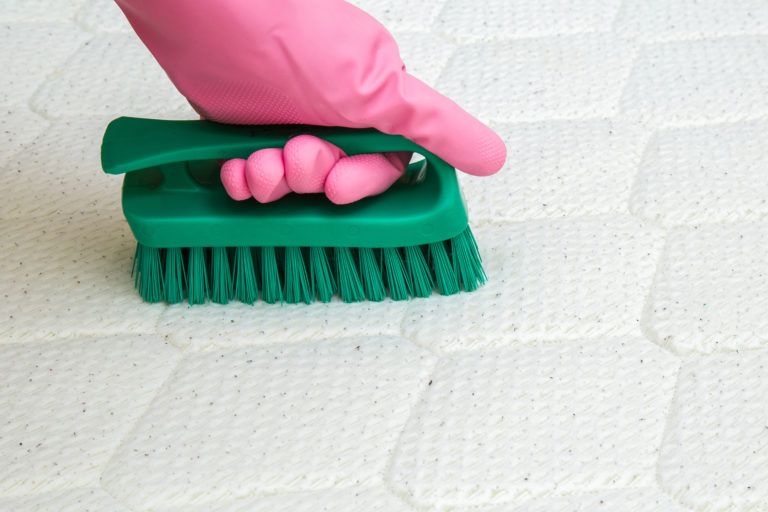 A gloved hand scrubs a mattress.