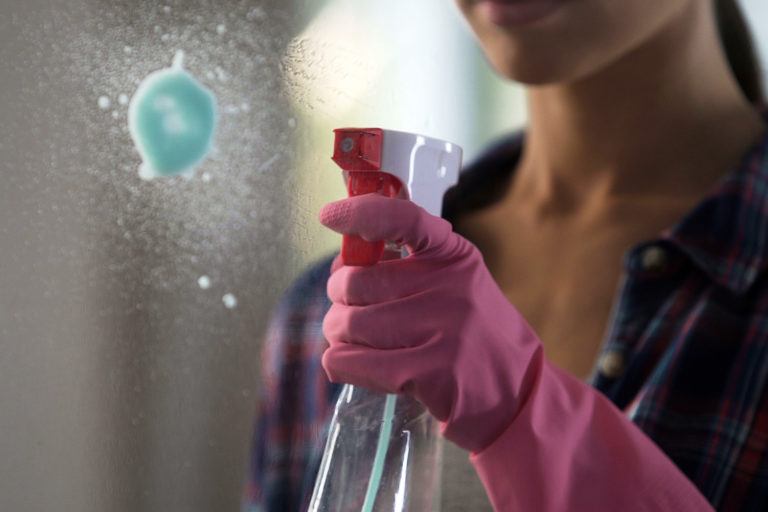 A woman sprays a mirror with glass cleaner.
