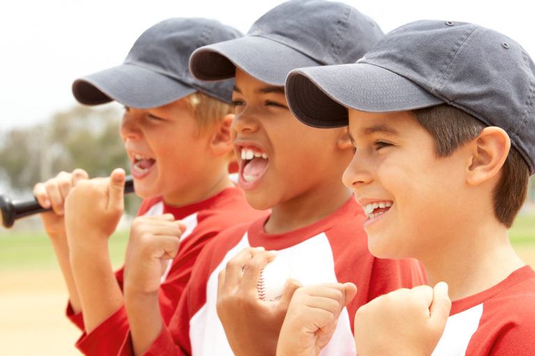 Three young boys with grey baseball hats on cheering at a baseball game.