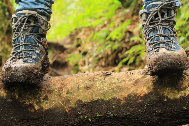 A person wearing muddy hiking boots standing on a log.