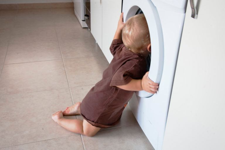 A baby inspecting a washing machine.