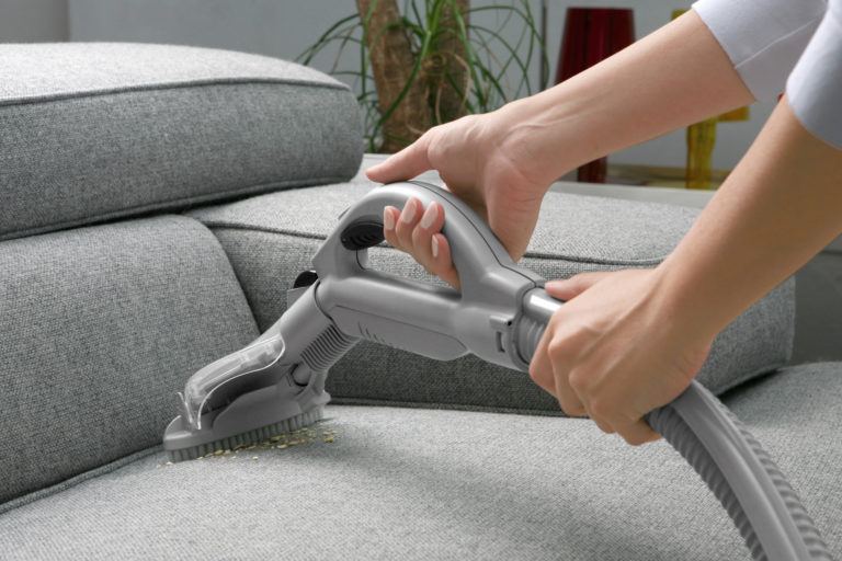 A person vacuuming a grey sofa.