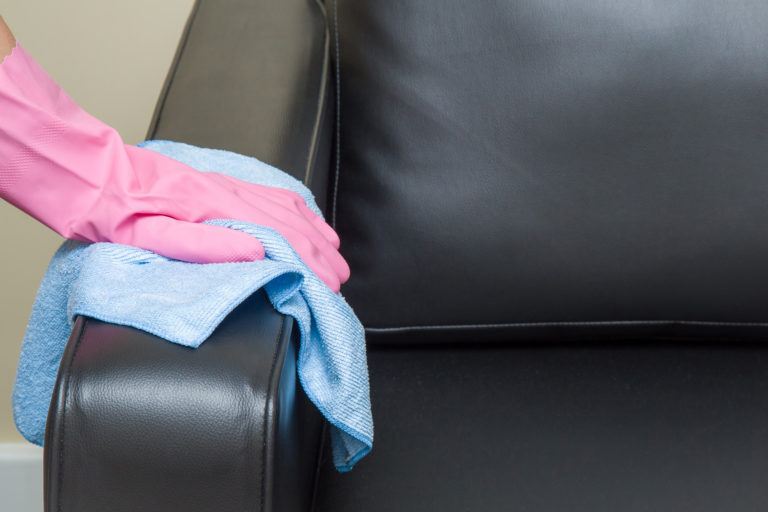 A person wiping down a black leather sofa with a blue microfiber cloth.