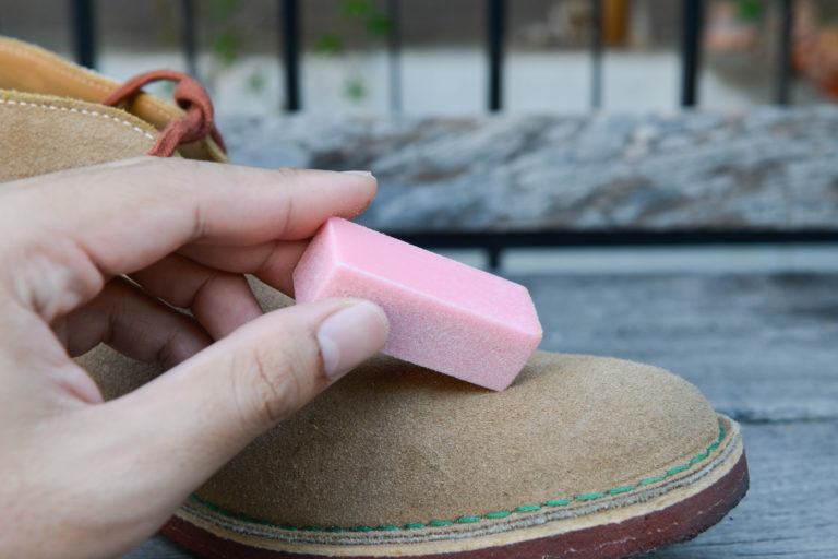 A person uses a suede eraser to clean their suede boots.