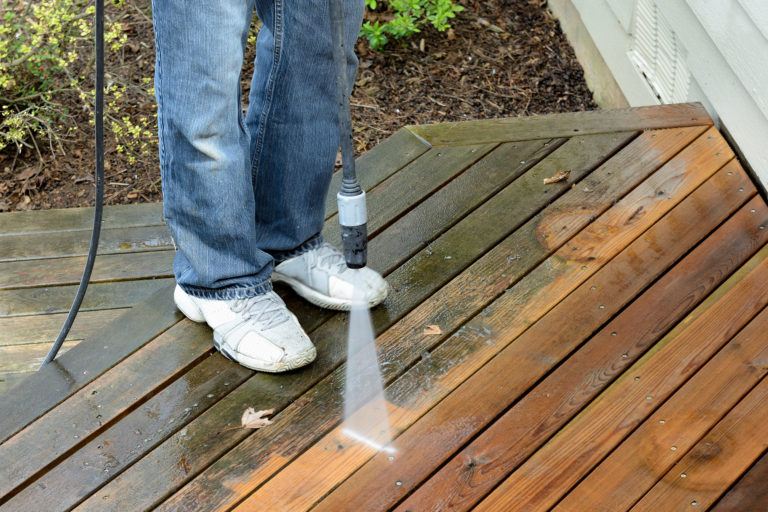 A person cleans a wooden deck with a pressure washer.