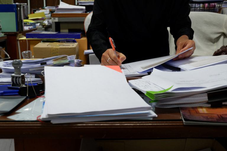 A person sits at a messy desk doing paperwork.