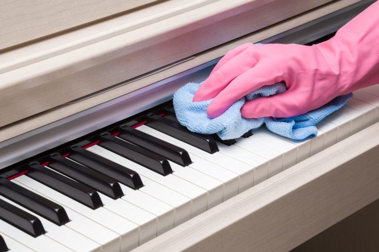 A gloved hand wiping down a piano with a microfiber cloth.