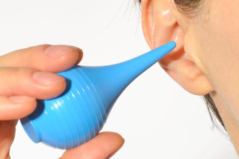 A person cleans holding a blue bulb syringe to their ear.