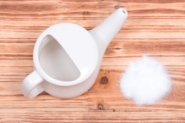 A neti pot with table salt sitting next to it.