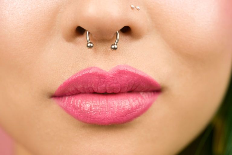 A nose piercing on a woman wearing bright pink lipstick.