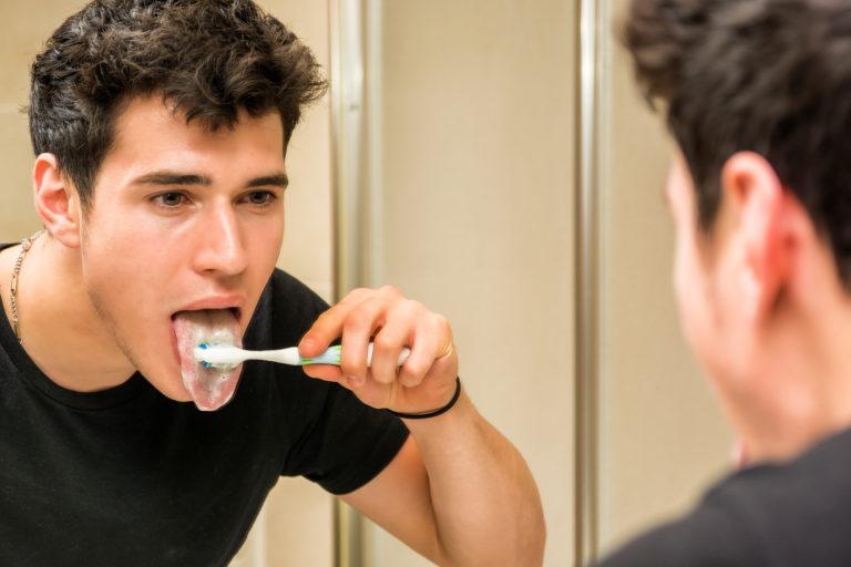 A man scrubbing his tongue with his toothbrush.