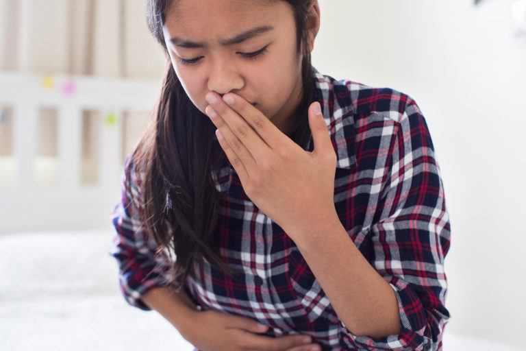 A girl holds her mouth and stomach trying not to vomit.