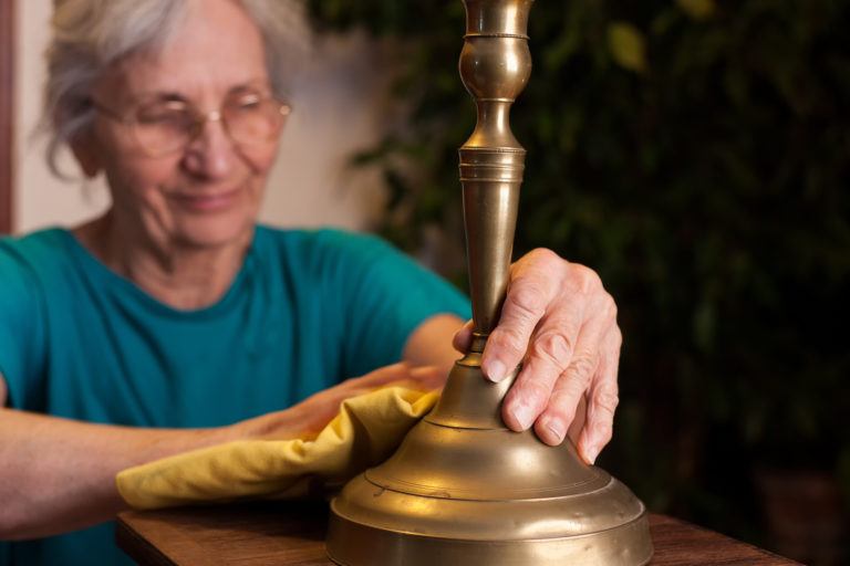 An elderly woman polishes a brass candlestick.