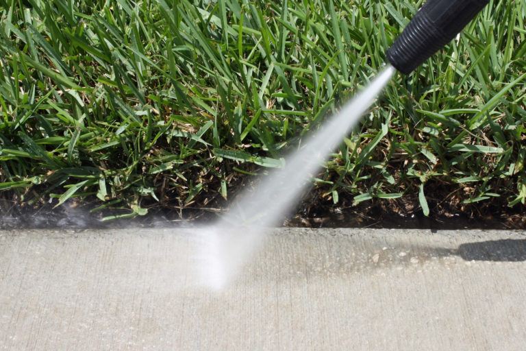 A concrete sidewalk is being cleaned by a power washer.