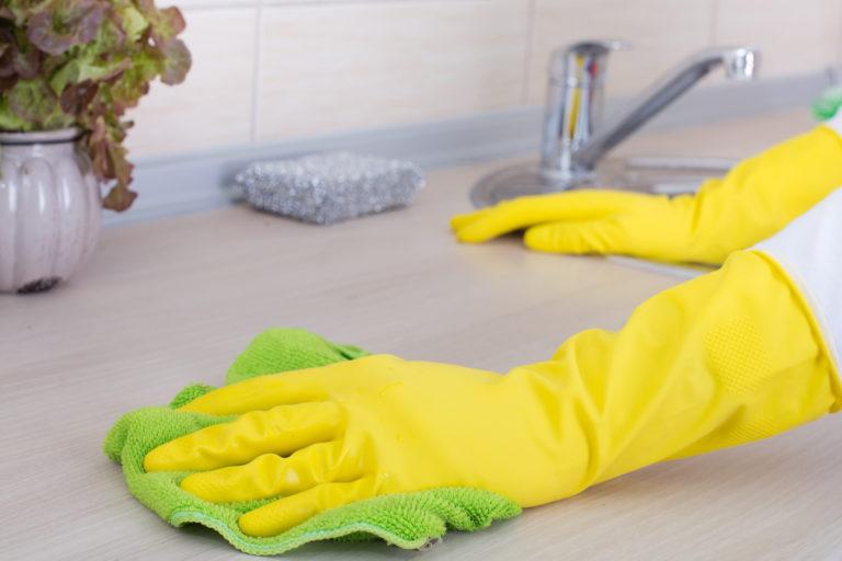 A gloved hand cleans a countertop with a cloth.