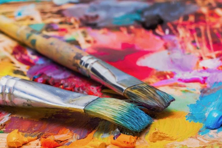 Artist paint brushes sitting atop lots of paint.