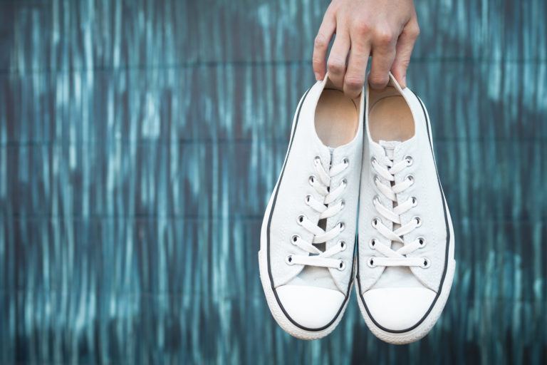 A person holding up a pair of clean white sneakers.